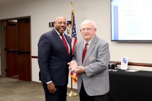 Photo of one man presenting an award to another man