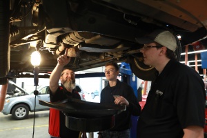 A photograph of two students working with a teacher on a car.