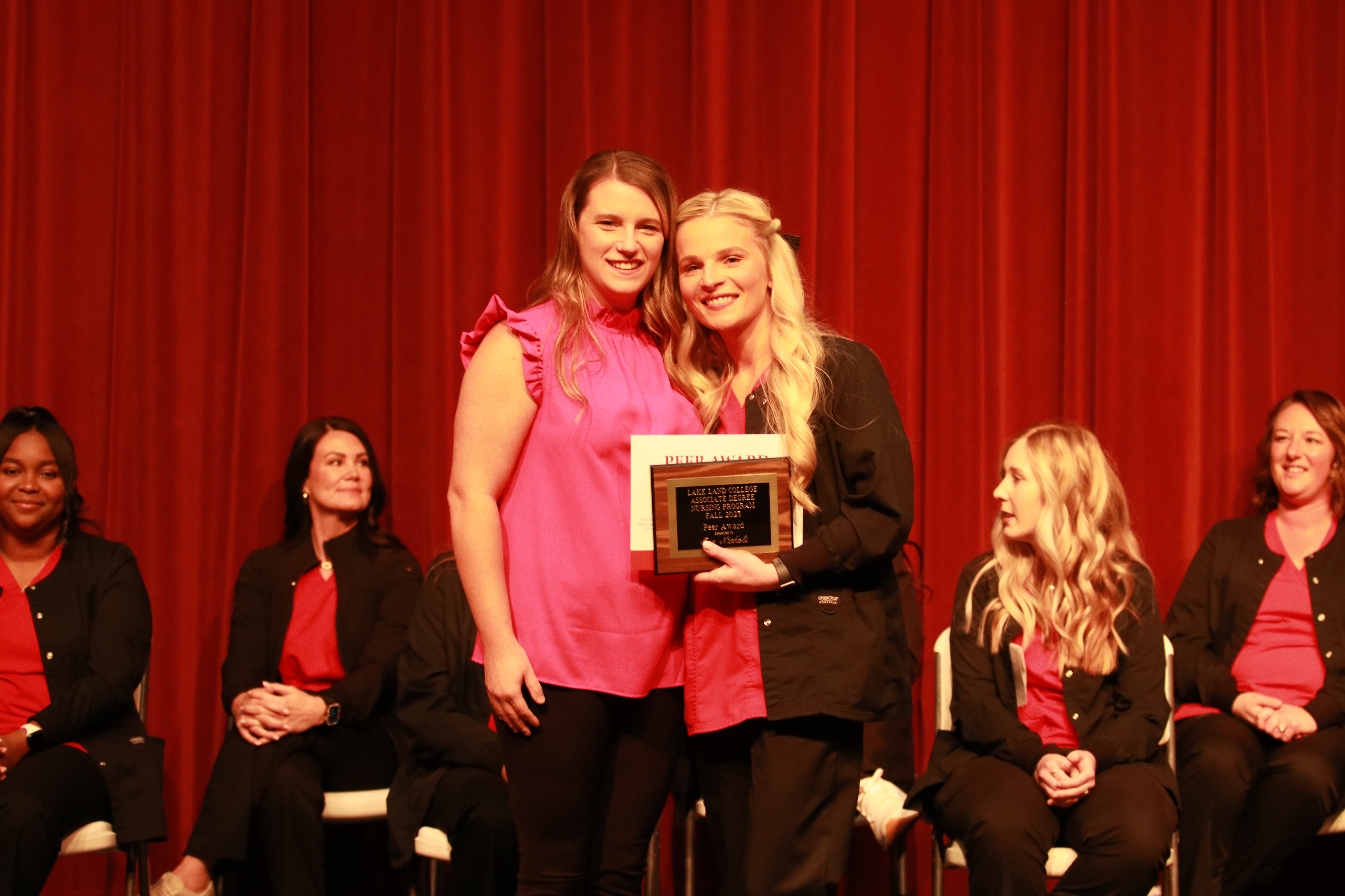 A nursing instructor presents an award to a graduating student at a ceremony. 