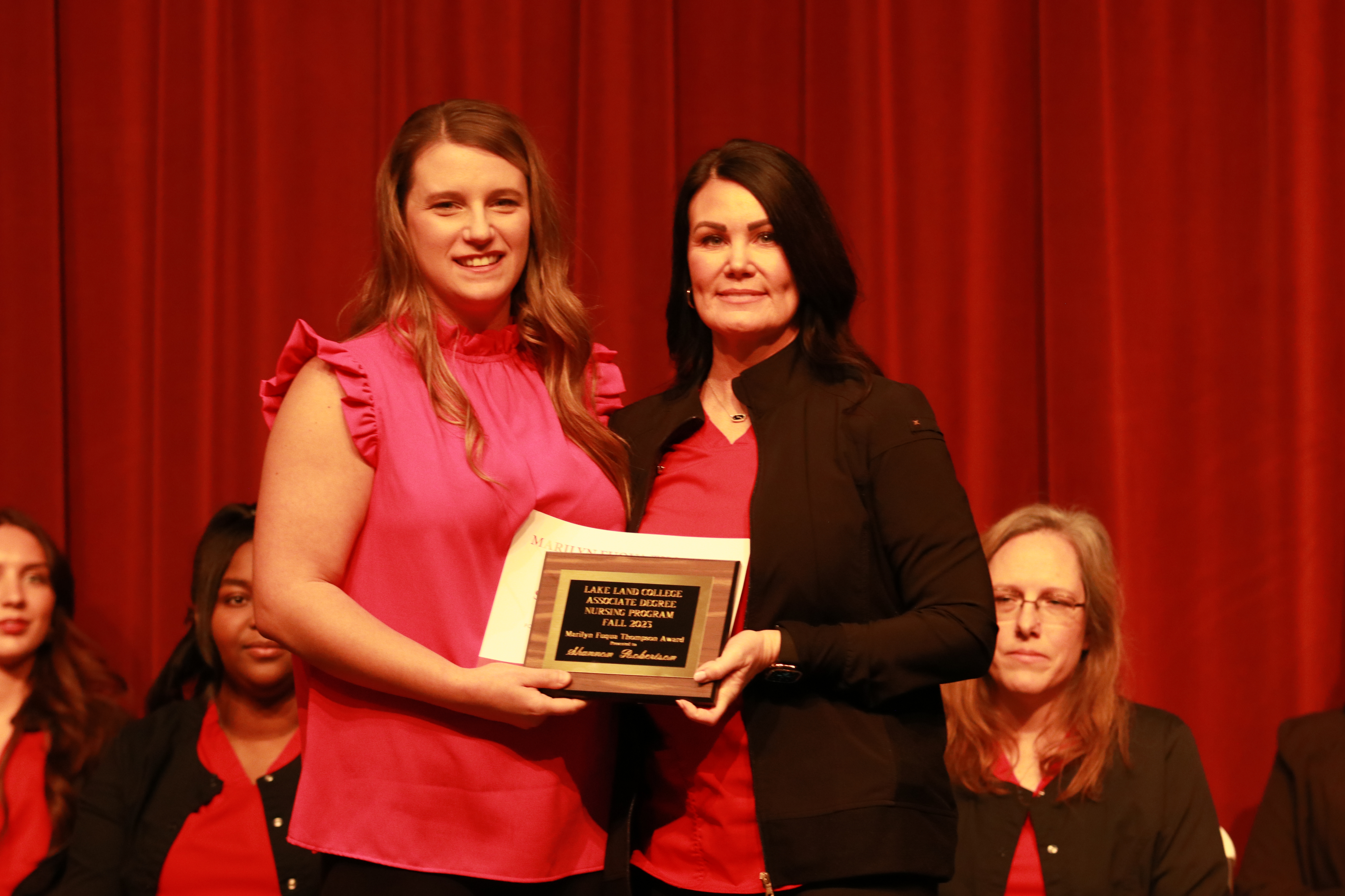 A nursing instructor presents an award to a graduating student at a ceremony. 