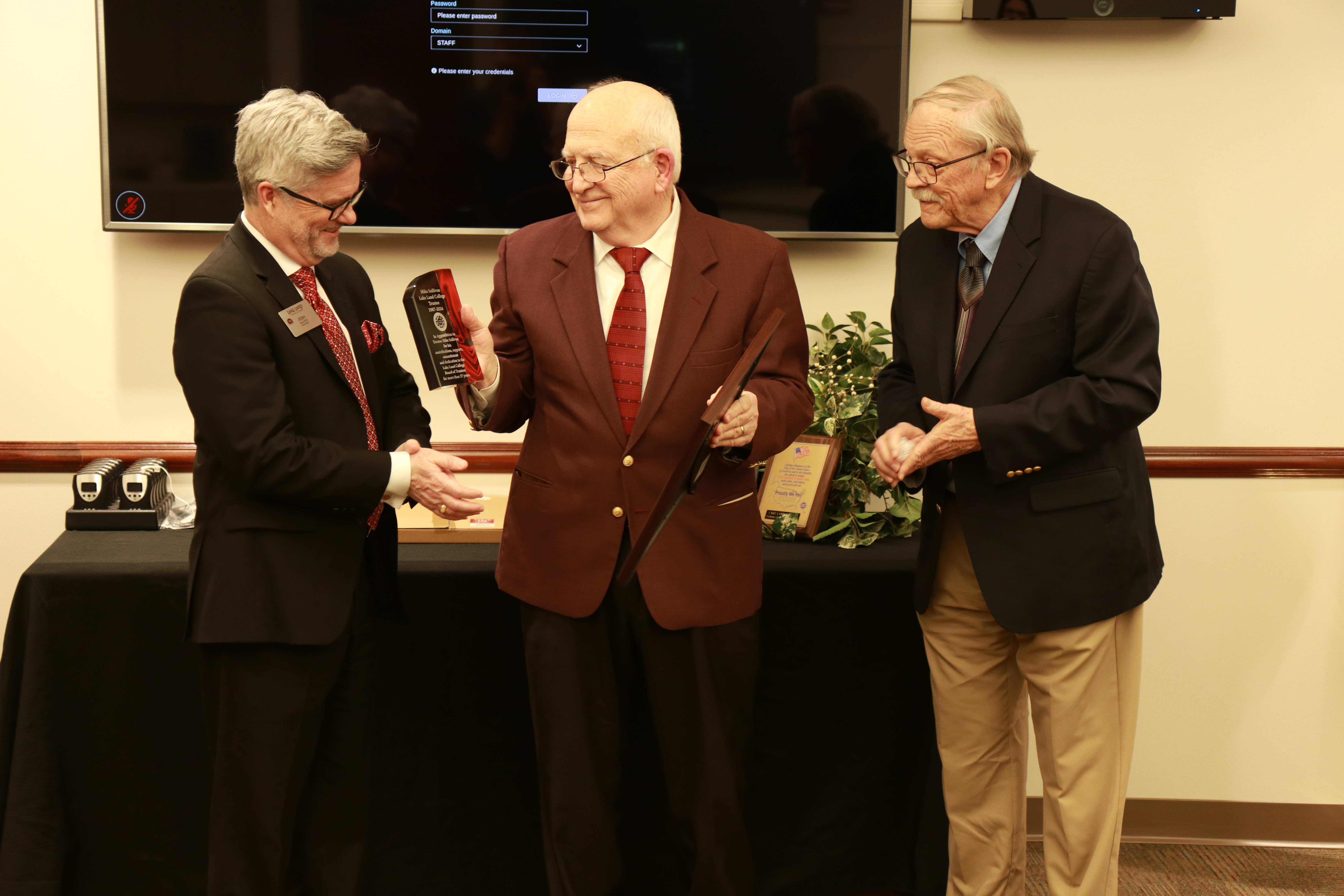 Three men, Lake Land College President Josh Bullock, former Lake Land College Trustee Mike Sullivan, and Lake Land College Board Chair Gary Cadwell, standing together as Bullock and Cadwell present Sullivan with a Resolution of Appreciation for his service. 