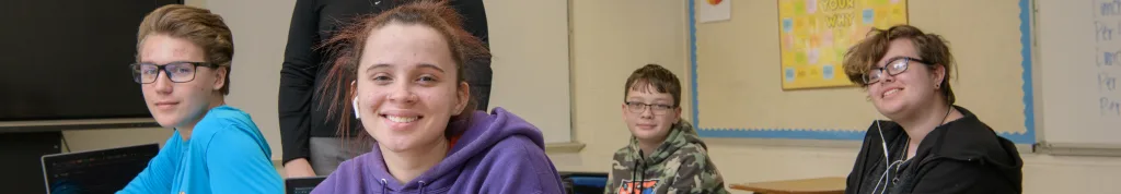 Four young students smiling at desks