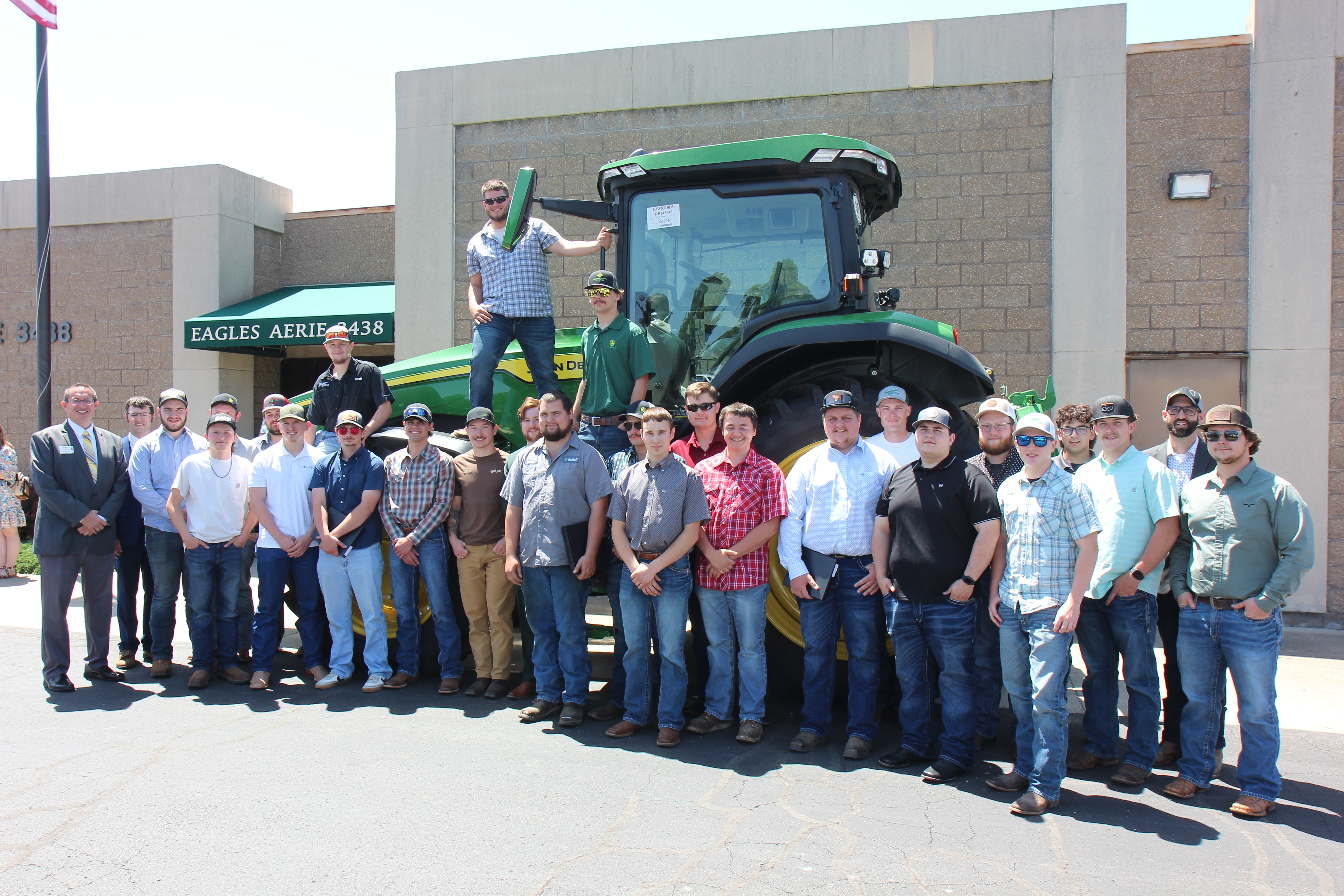 John Deere Tech students and instructors gathered around a John Deere tractor. 