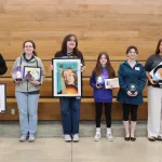 Students and staff members holding awards and artwork while posing for a photo