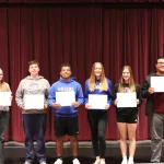 Students holding certificates and posing for a photo on a stage