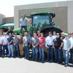 Students posing for a photo standing in front of a tractor