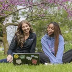 Photo of two students sitting outside looking at a laptop.
