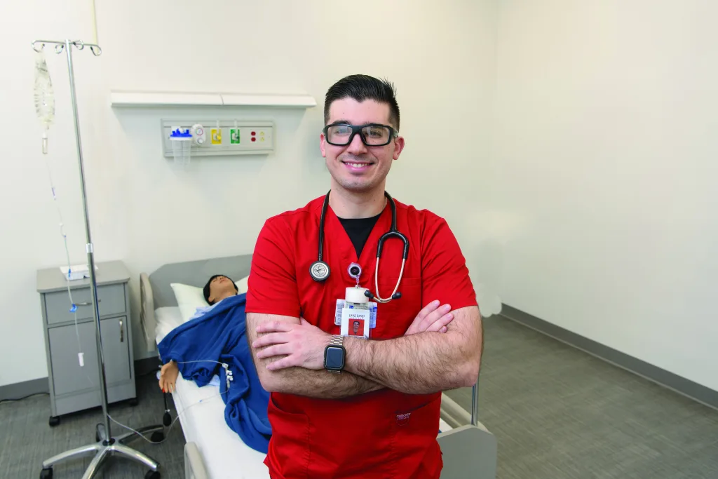 Nursing student standing with arms crossed, posing for a photo in front of a hospital bed