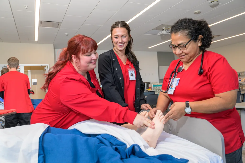 A photograph of two ADN students working with a teacher in a nursing lab.