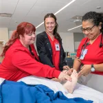 A photograph of two ADN students working with a teacher in a nursing lab.