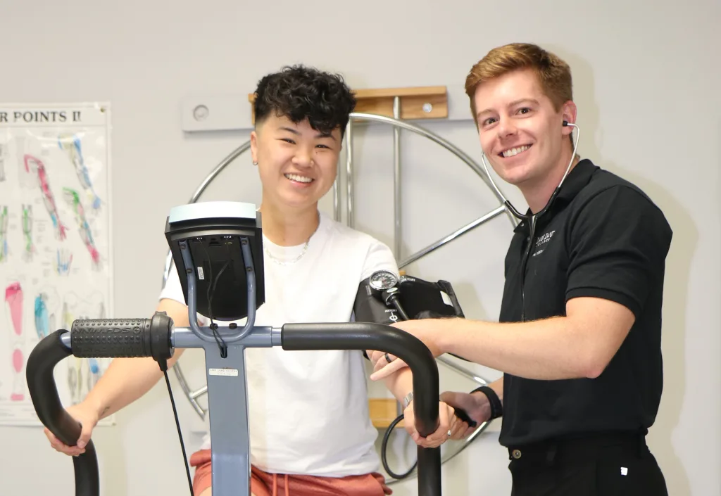 A photograph of two physical therapist students using equipment and smiling at the camera.