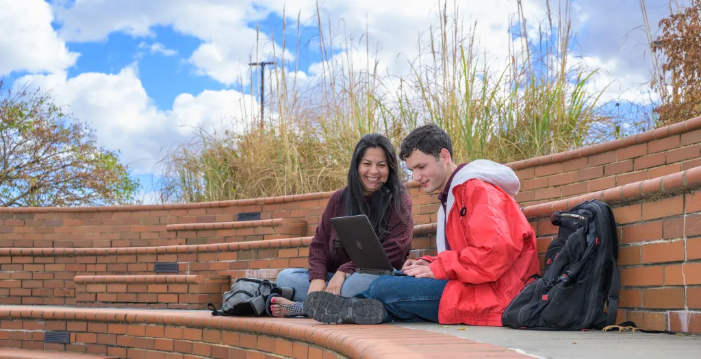 Two students sitting outside and working on a laptop.