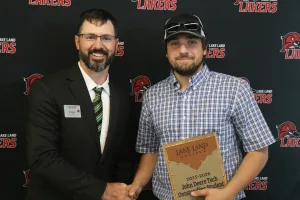 An instructor presenting the 2025-2026 John Deere Tech Outstanding Student Award to a student during the annual Lake Land College John Deere Tech graduation ceremony.