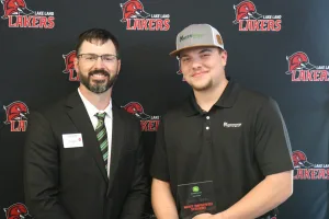 An instructor presenting the 2025-2026 Most Improved Student Award to a student during the annual Lake Land College John Deere Tech graduation ceremony. 
