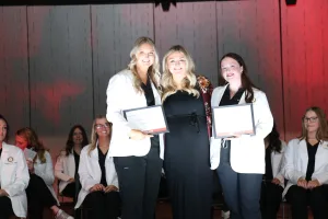 Two dental hygiene students receiving awards from an instructor during a graduation ceremony.
