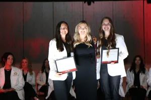 Two dental hygiene students receiving awards from an instructor during a graduation ceremony.